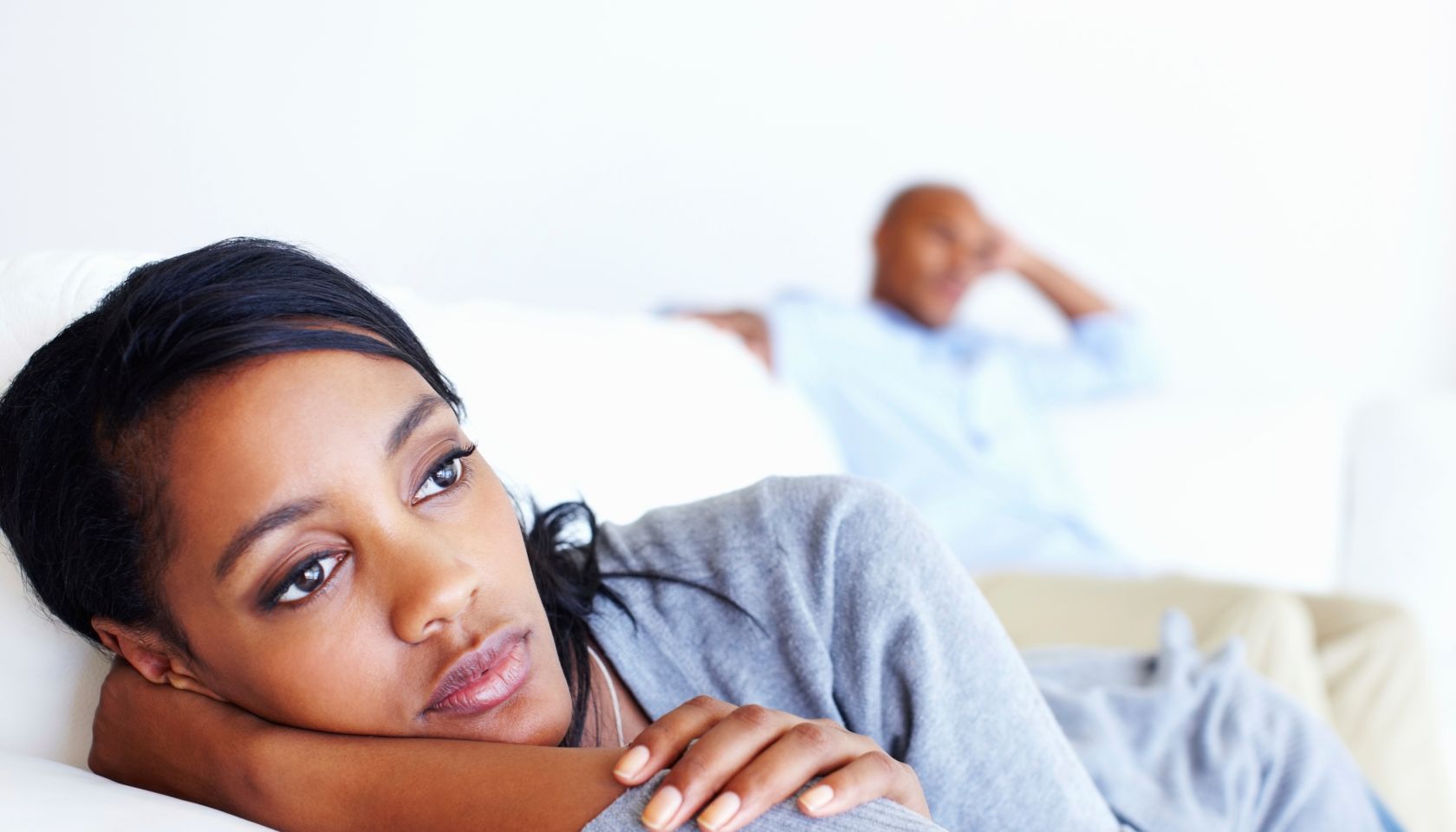 An unhappy couple sitting on opposite ends of a sofa