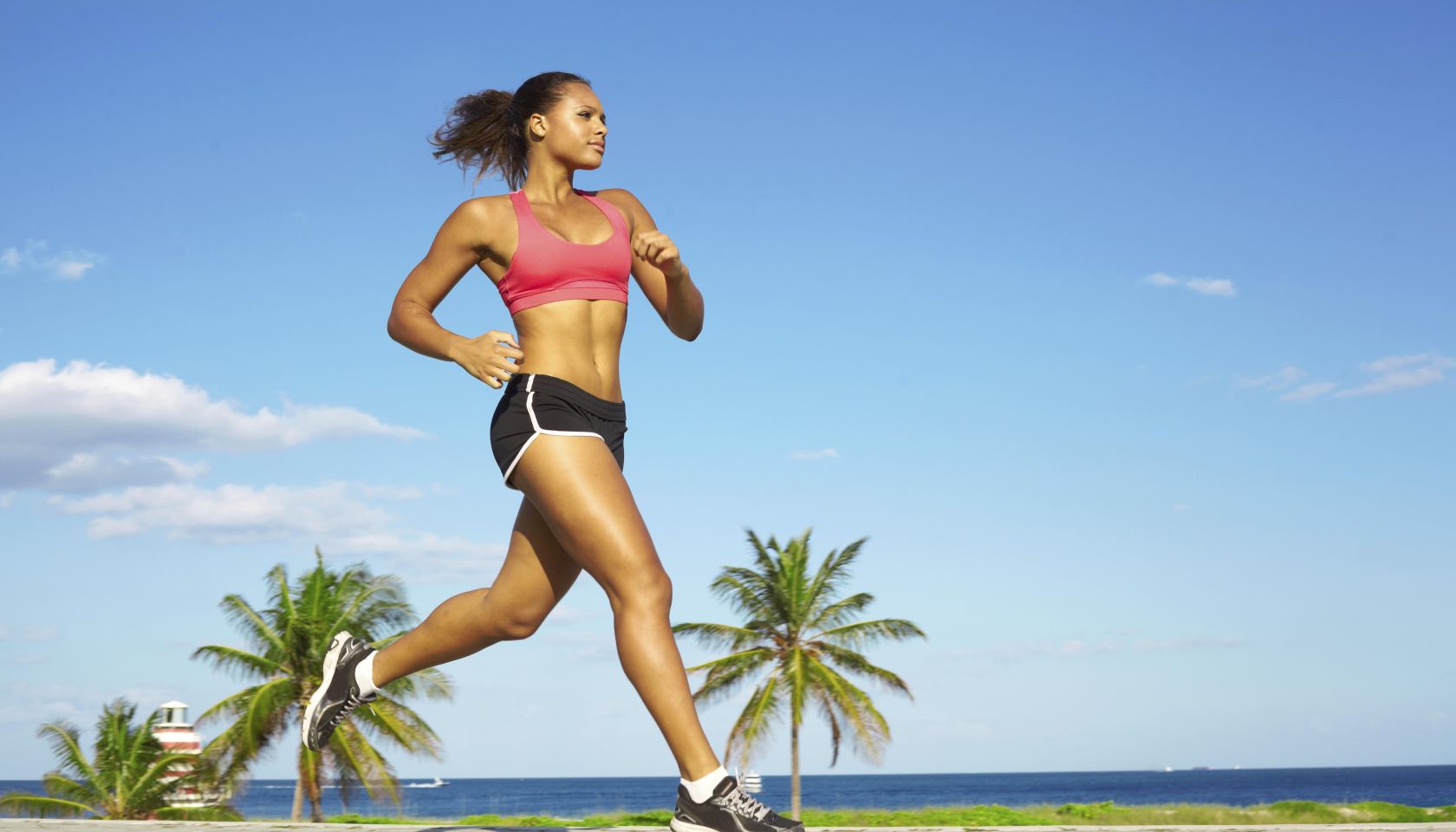 Sporty mixed race woman jogging. Color image, copy space, african american ethnicity female running with green grass and blue sky.