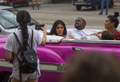 CORRRECTS NAME OF KANYE WEST - A woman uses her cellphone to take a picture American reality-show star Kim Kardashian West, center, and her husband Kanye West as they ride on a classic car along the streets of Havana, Cuba, Wednesday, May 4, 2016. Rap superstar Kanye West, his wife Kim Kardashian and members of her reality-show-star family have become the latest celebrities to visit Havana. They visited Havanas Museum of Rum Wednesday, stepping out of a hot-pink antique American convertible as they snapped selfies and were recorded by a television crew following them around. At right is Kourtney Mary Kardashian,(AP Photo/Desmond Boylan)