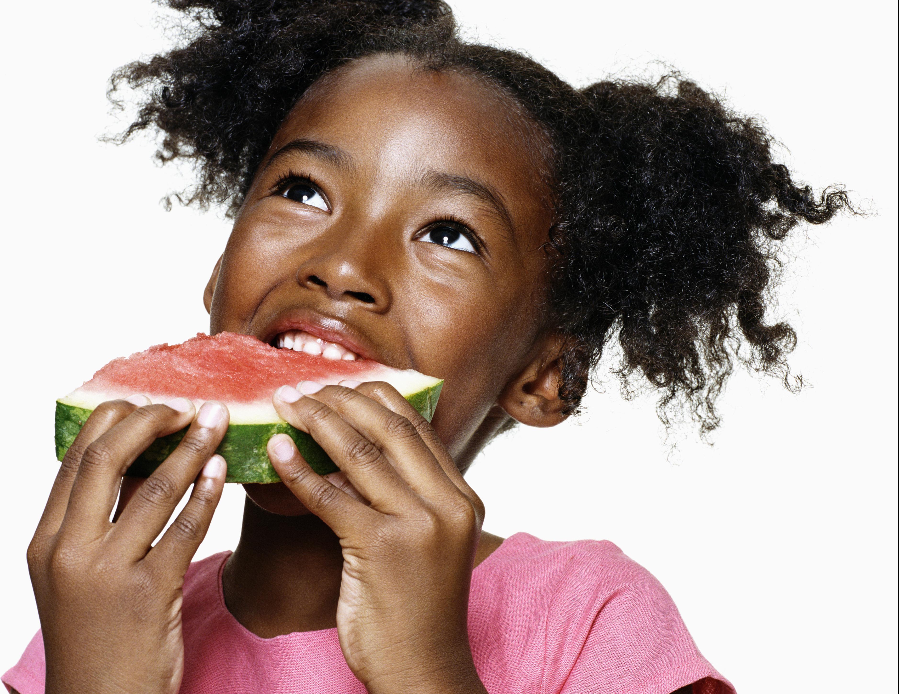 Girl (6-7) looking upwards eating watermelon, close-up