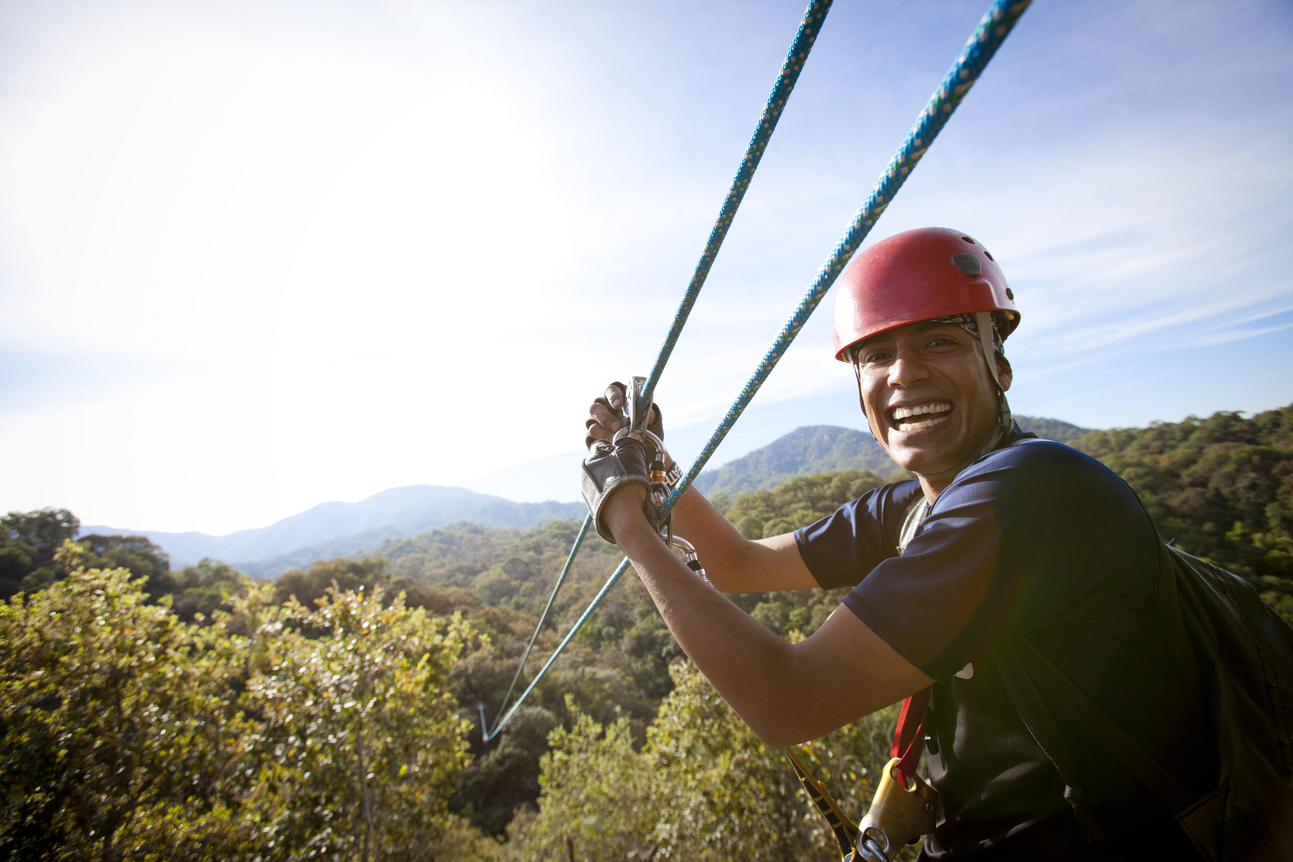 Guy smiling with hands on zip line over tree tops