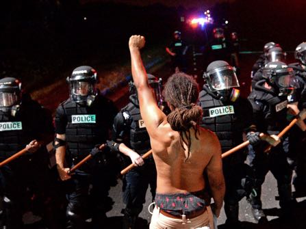 A protester stands with his left arm extended and fist clenched in front of a line of police officers in Charlotte, N.C. on Tuesday, Sept. 20, 2016. Authorities used tear gas to disperse protesters in an overnight demonstration that broke out Tuesday after Keith Lamont Scott was fatally shot by an officer at an apartment complex. (Jeff Siner/The Charlotte Observer via AP)