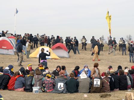 FILE - In this Oct. 27, 2016 file photo, Dakota Access Pipeline protesters sit in a prayer circle at the Front Line Camp as a line of law enforcement officers make their way across the camp to remove the protesters and relocate to the overflow camp a few miles to the south on Highway 1806 in Morton County, N.D. Members of more than 200 tribes from across North America have come to the Standing Rock Sioux Tribe's encampment at the confluence of the Missouri and Cannonball rivers since August, the tribe says. Estimates at the protest site have varied from a few hundred to several thousand depending on the day _ enough for tribal officials to call it one of the largest gatherings of Native Americans in a century or more. (Mike McCleary/The Bismarck Tribune via AP, File)