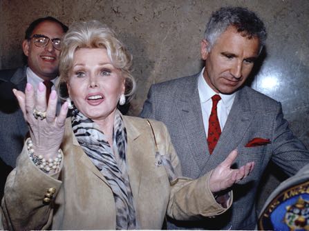 FILE - In a May 1, 1990 file photo, Zsa Zsa Gabor gestures as she while answering questions as she leaves the Beverly Hills courtroom where judge Charles Rubin ruled that she violated her probation. Gabor was ordered to complete her community service at a Venice homeless shelter, with an additional 60 hours. At right is her husband Frederick von Anhalt. Gabor died Sunday, Dec. 18, 2016, of a heart attack at her Bel-Air home, her husband, Prince Frederic von Anhalt, said. She was 99.(AP Photo/Kevork Djansezian, File)