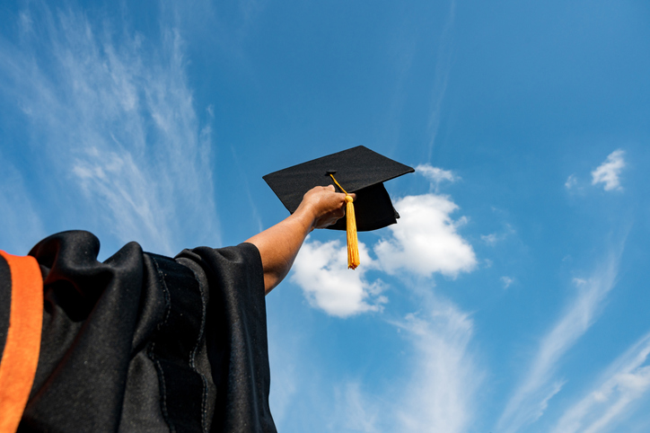 Cropped Hand Of Person Holding Mortarboard Against Blue Sky