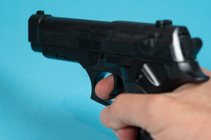 A person (man) holds a gun that he is about to shoot pointing at someone or something.