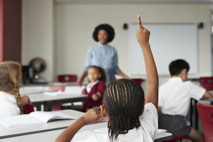 Focus on schoolgirls raised hand in classroom with teacher