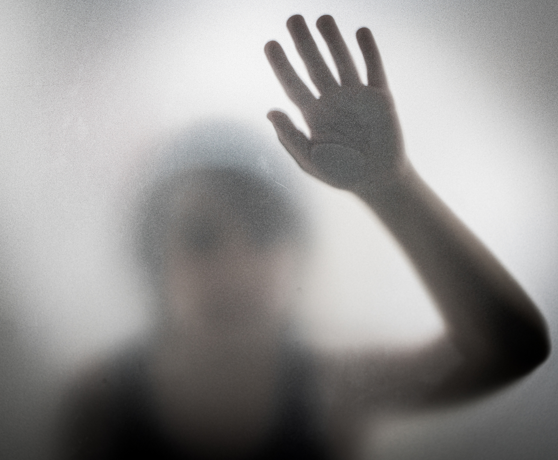 Little defocused boy in shadow behind glass