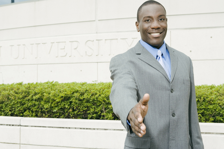 Smiling Man in Suit Standing in Front of "University" Sign