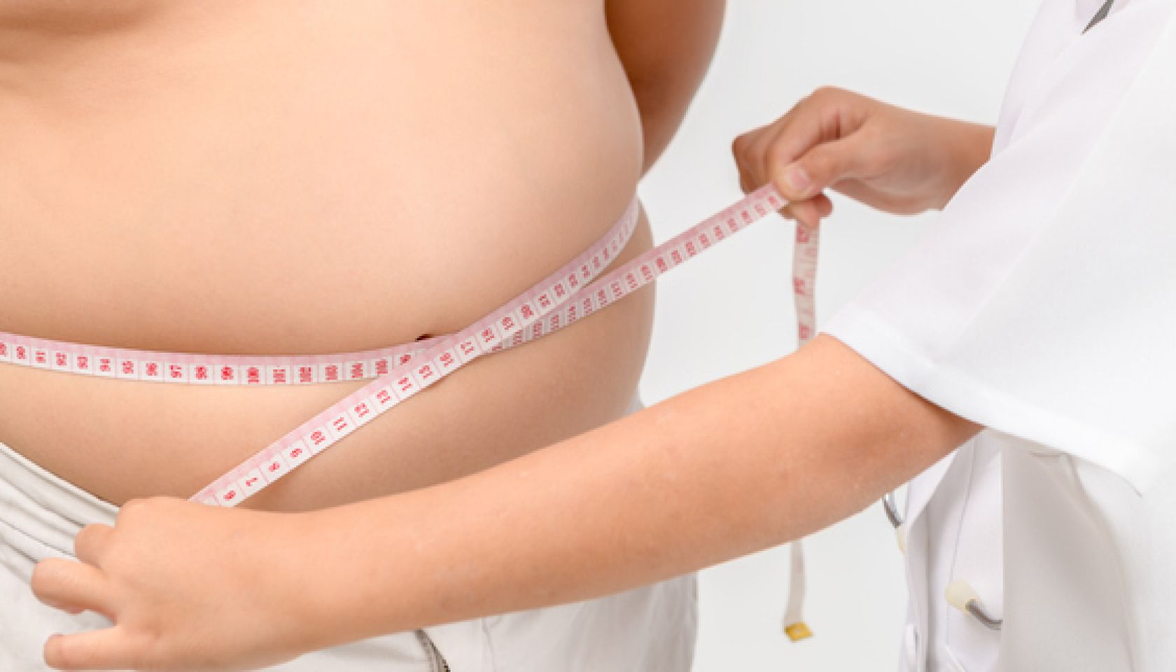 Midsection Of Doctor Measuring Abdomen Of Patient Against Gray Background