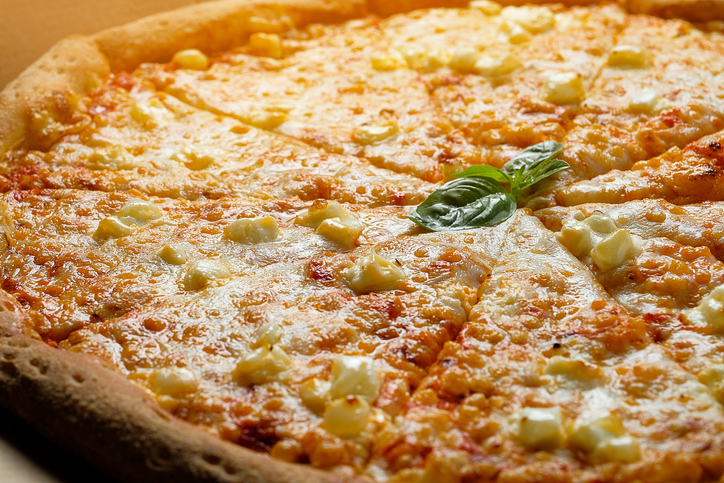 Italian pizza in a pizza box and for delivery, on a white background or table. Pizza Margarita with tomatoes and cheese, cut into pieces, without meat. The concept of Vegetarian food, fast unhealthy food. Delivery to your home or work. Copy space.