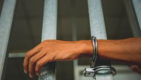 Cropped Hand Of Man Handcuffed To Bars At Prison