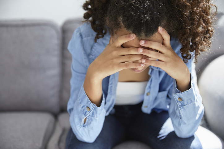 Sad and unhappy teenager sitting in sofa covering her face with her hands