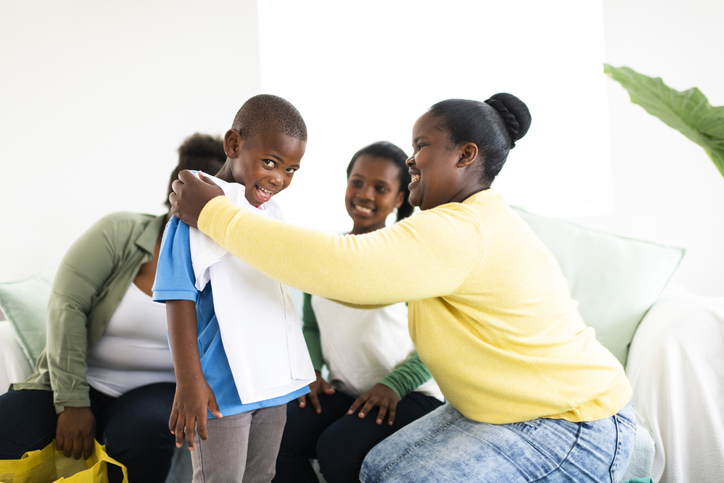 Mother holds new school shirt against excited boys chest