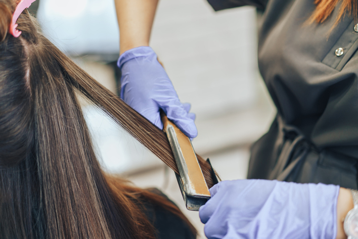 Close-up of a hairdresser straightening long brown hair with hair irons