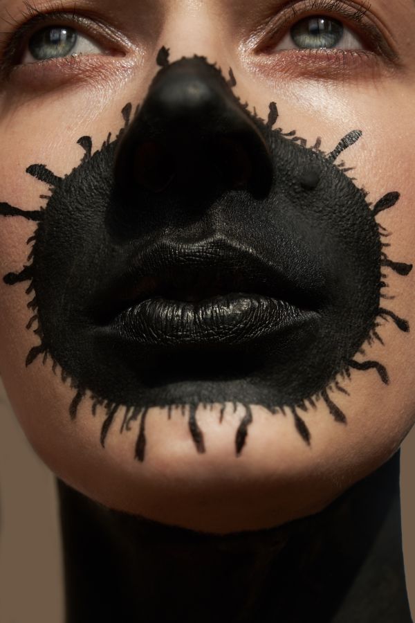Close up portrait of a beautiful woman with black virus painting on her face like a face mask. The young woman with blue eyes is looking away. The concept of virus, isolation, loneliness, virus in the network, fear, infection, halloween makeup.