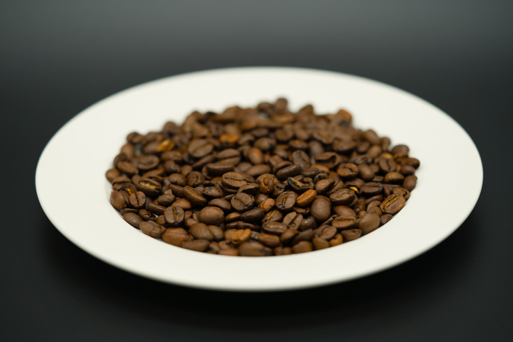 White plate full of aromatic coffee beans against a dark background