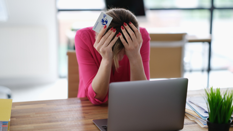 Upset woman sitting at laptop with credit plastic card and holding his head