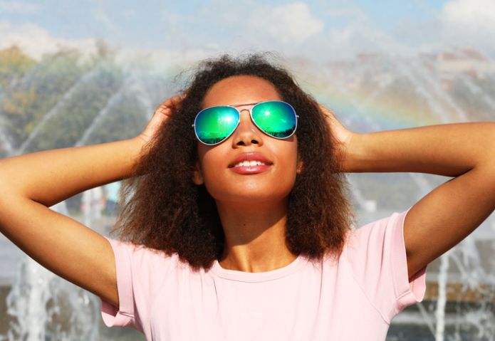 woman wearing sunglasses with perfect teeth and dark clean skin having rest outdoors