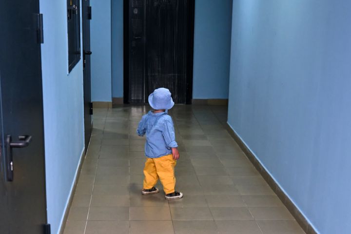 The toddler baby walks in the entrance hall on the floor near the apartment doors. A child runs in the hallway of an apartment building. Kid aged about two years (one year eleven months)