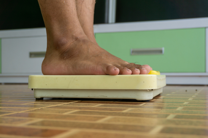 Standing on floor scale. Close up of man legs stapping on weight scales.