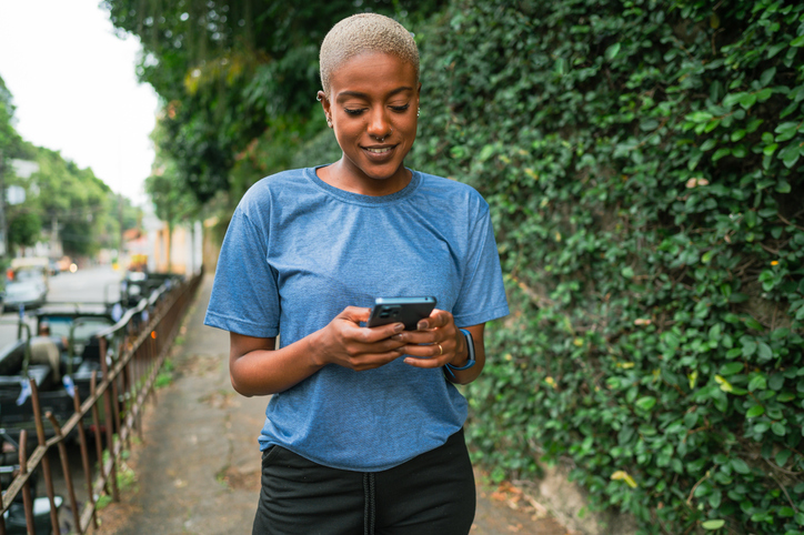 A happy woman on the street using her cell phone after her walk