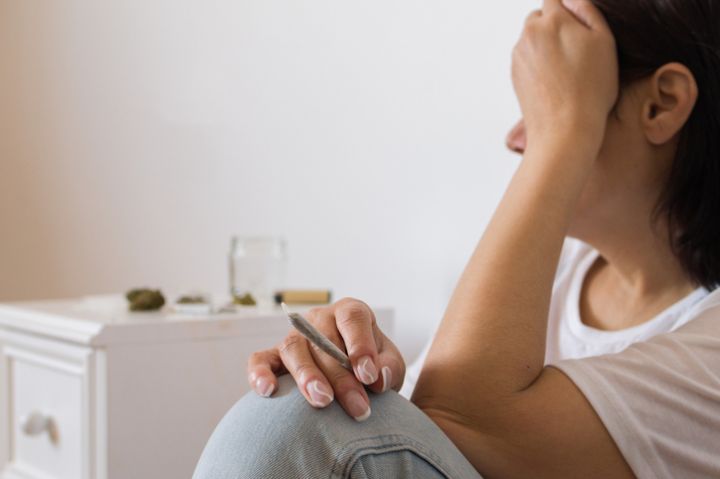 unrecognizable woman with drug addiction holding a rolled joint of cannabis in her hand next to a stash of bud. concept of smoking marijuana
