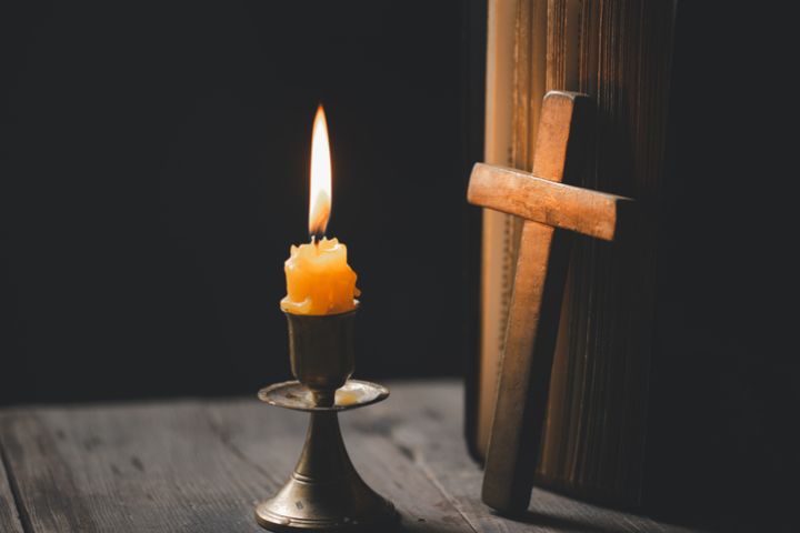 Light candle with holy bible and cross or crucifix on old wooden background in church.Candlelight and open book on vintage wood table christianity study and reading in home.Concept of christ religion