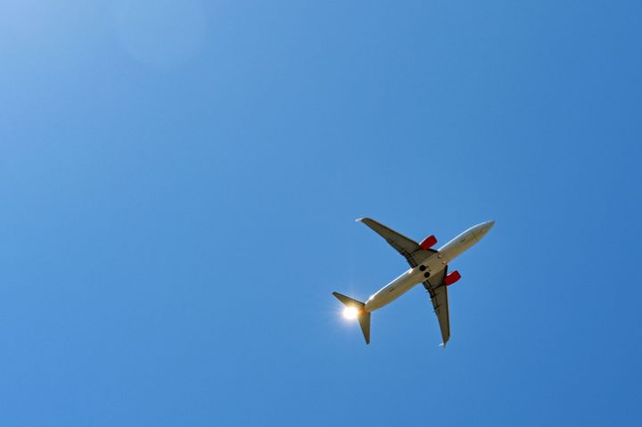 Holiday jet in flight seen from below with sun lighting up the plane's tail