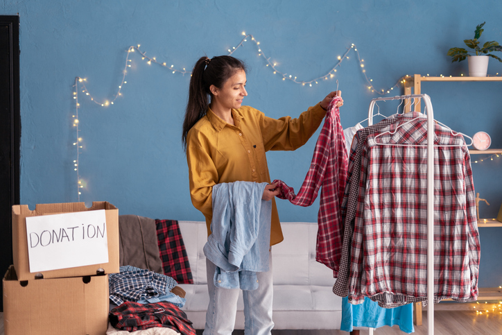 Second-hand concept. Latin woman selecting clothes from her wardrobe for donating to a charity center. Sorting clothes and cleaning-up.