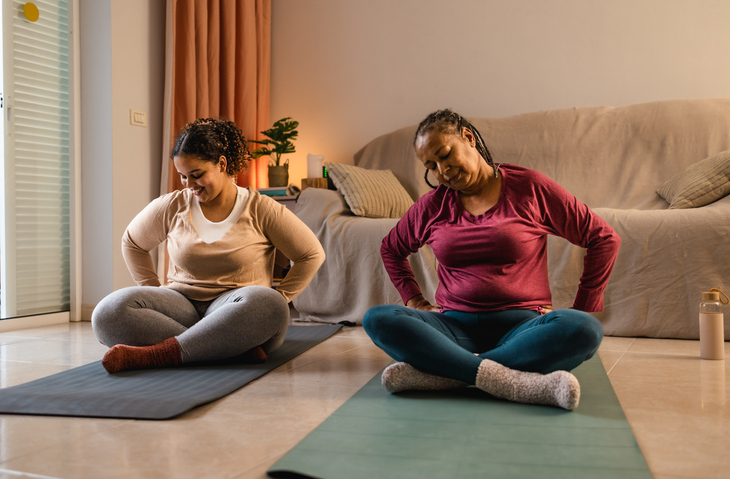 Happy African mother with her daughter doing yoga at home