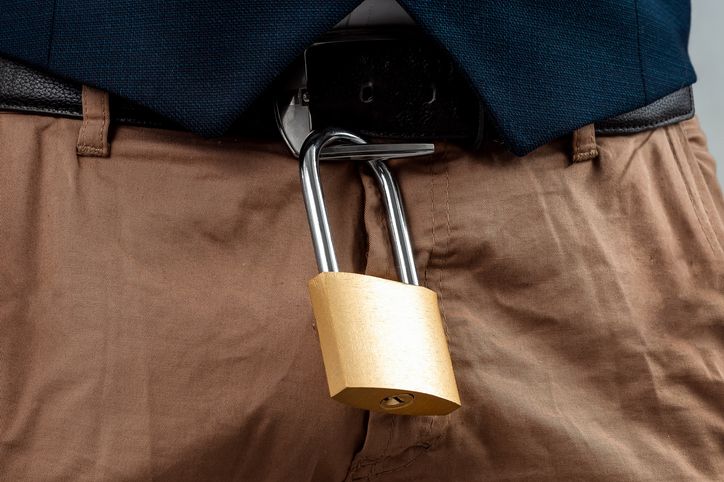 Close-up of a gold padlock hanging from a man's belt. The concept of marital fidelity, celibacy, treason, chastity belt.