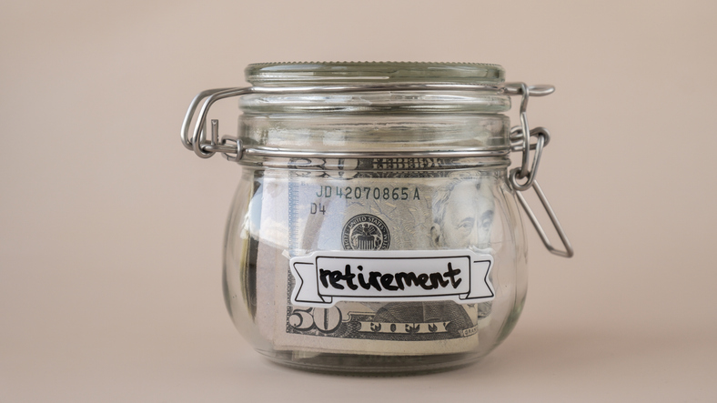 Saving Money In Glass Jar filled with Dollars banknotes. RETIREMENT transcription in front of jar. Managing personal finances extra income for future insecurity