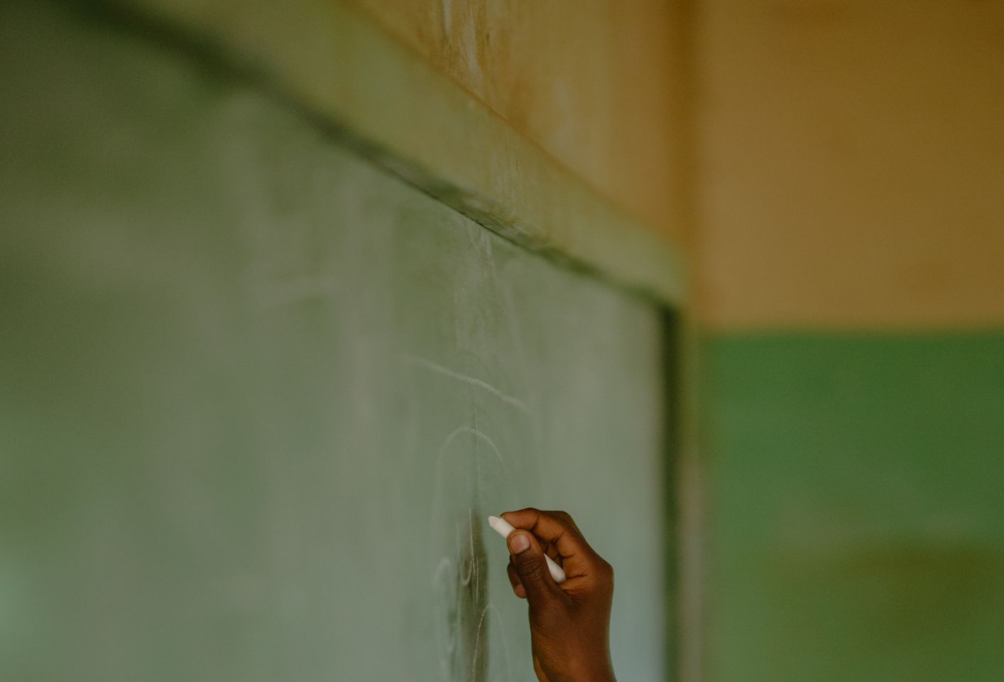 African Schoolboy Learner's hand holding chalk at chalkboard in a rural school classroom