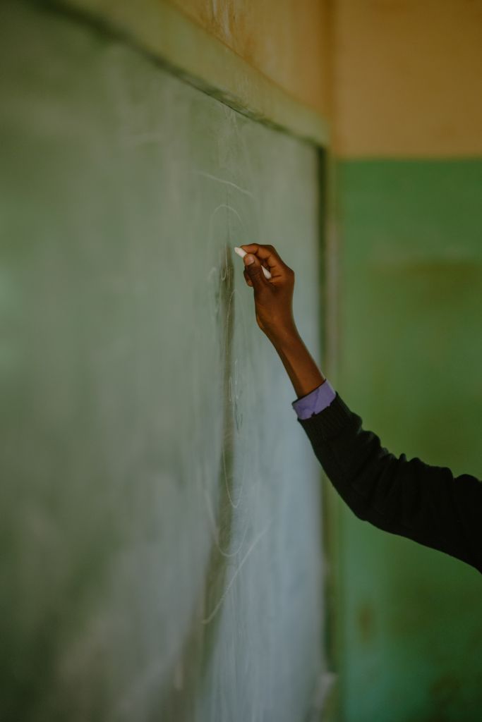 African Schoolboy Learner's hand holding chalk at chalkboard in a rural school classroom