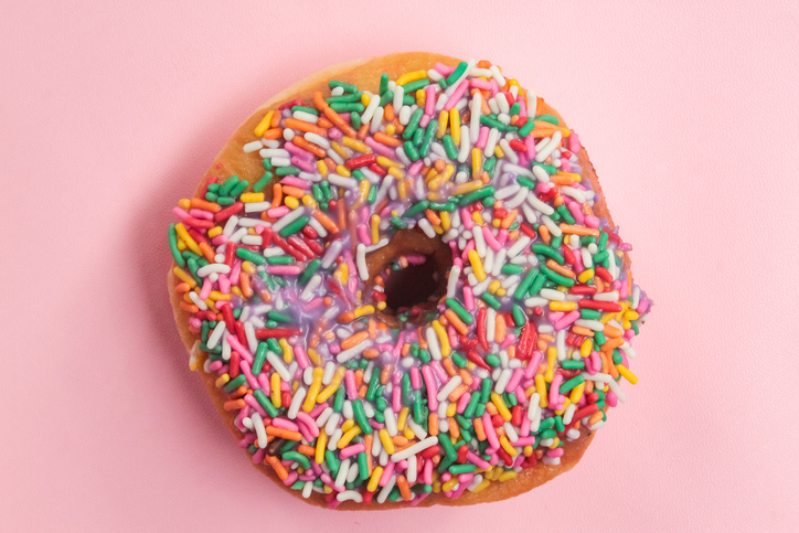 a donut with colorful chocolate sprinkles on a pink background