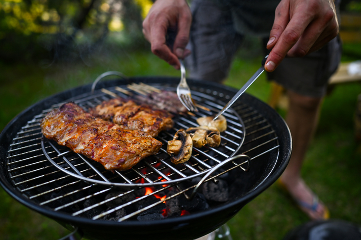 Person grilling meat and mushrooms on outdoor barbecue