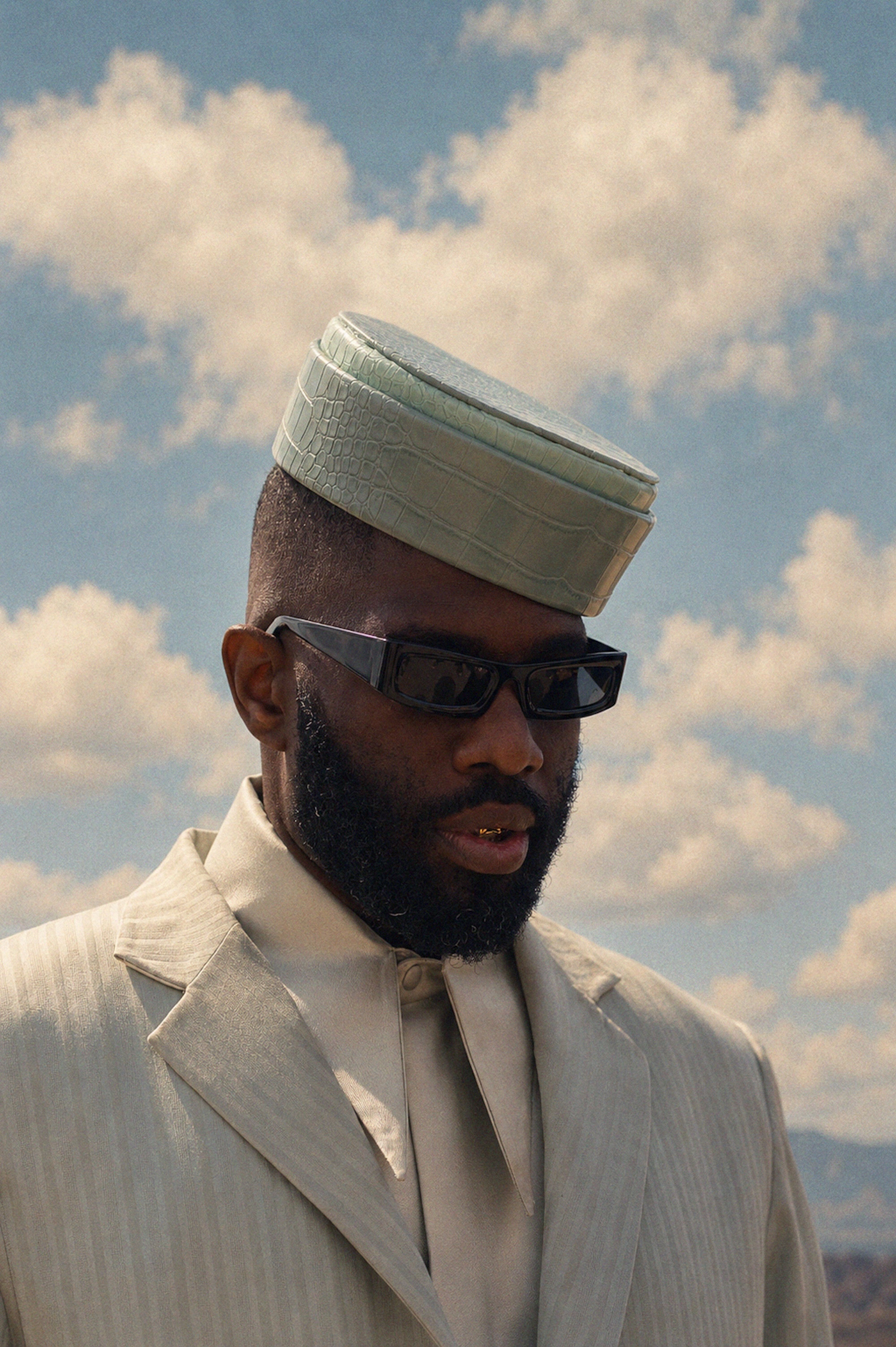 A man wearing a white robe and turban, with a beard, standing against a cloudy sky.