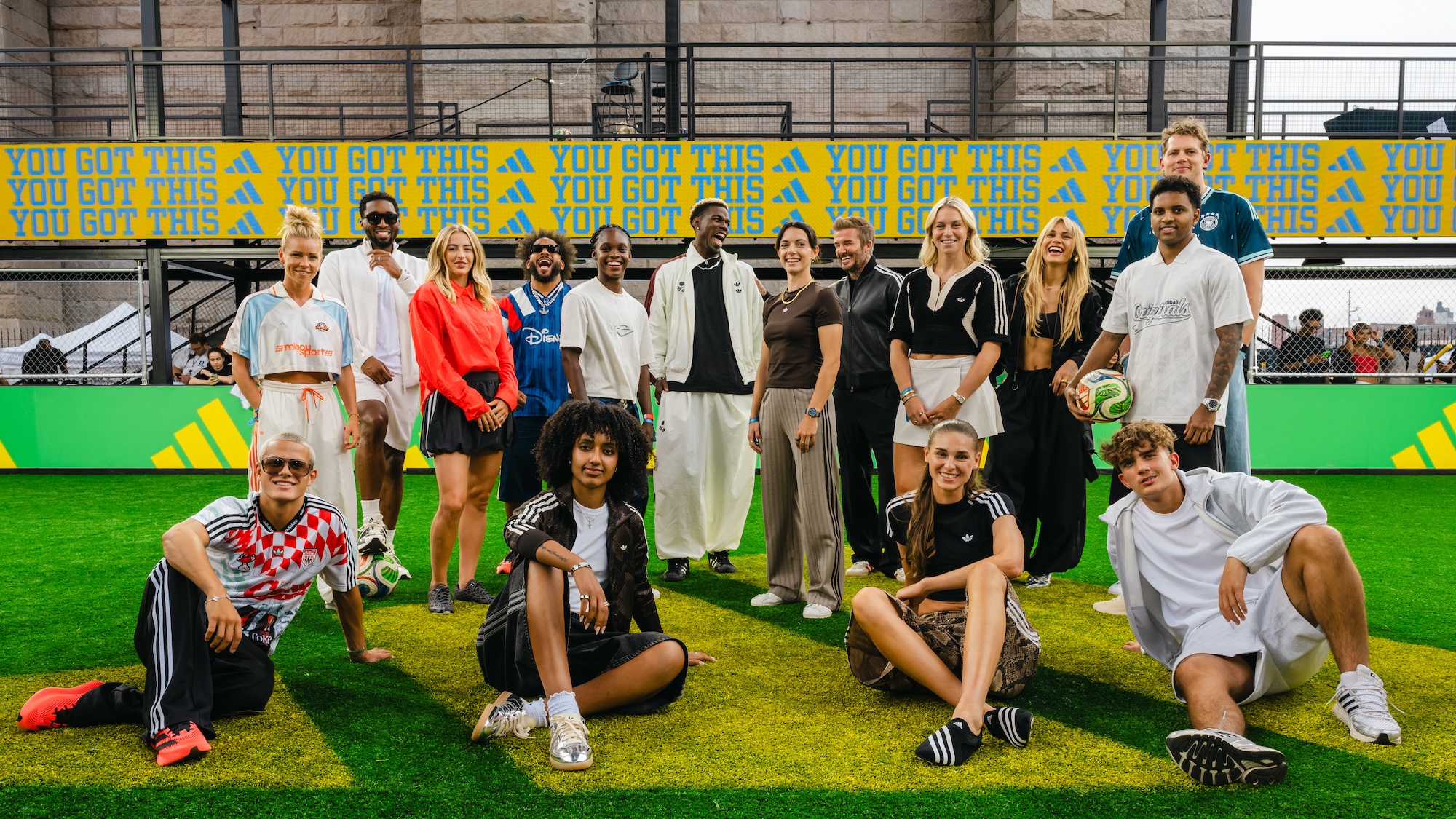 A group of diverse people posing together on a green artificial turf field, with "You got this" banners in the background.