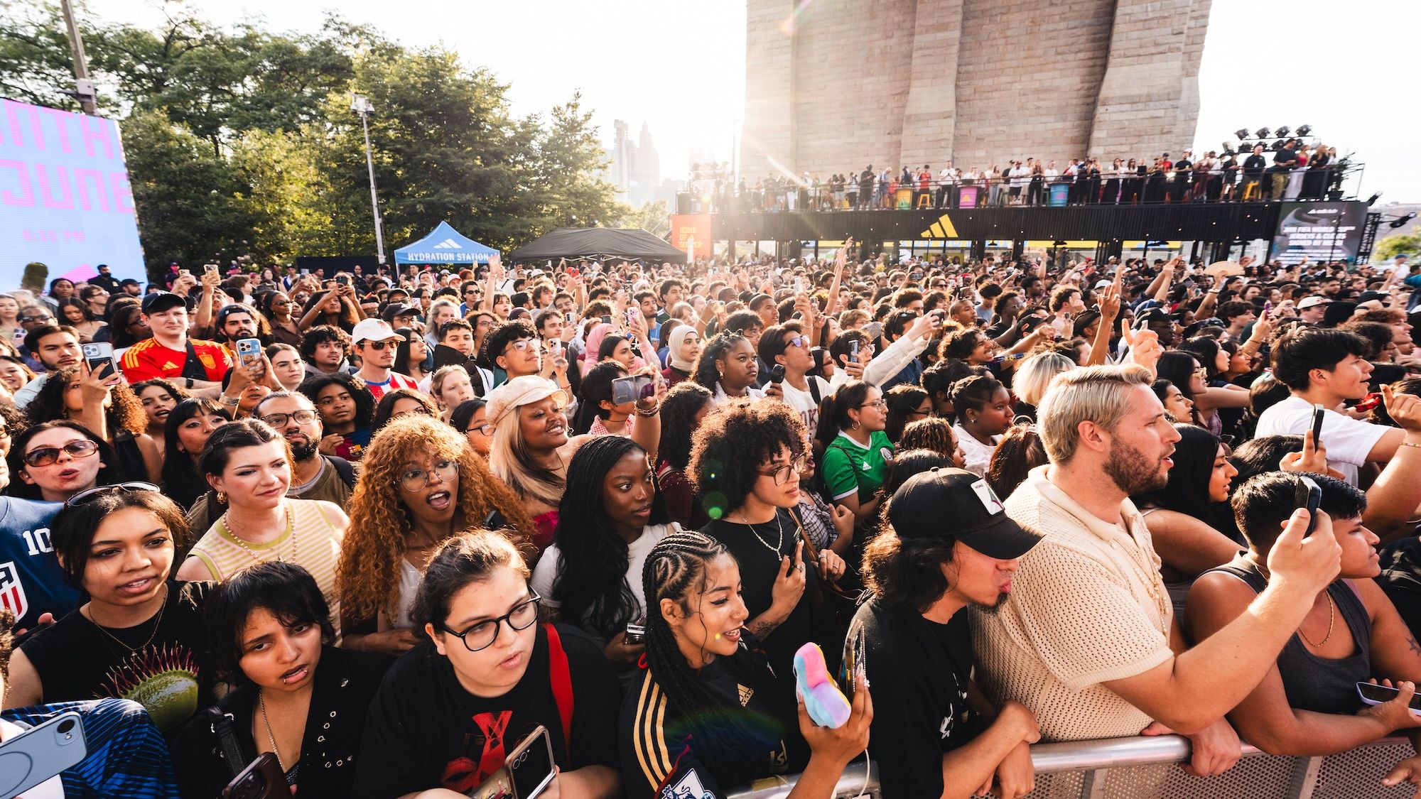 A large crowd of people gathered at an outdoor event, with many holding up their phones and cheering.