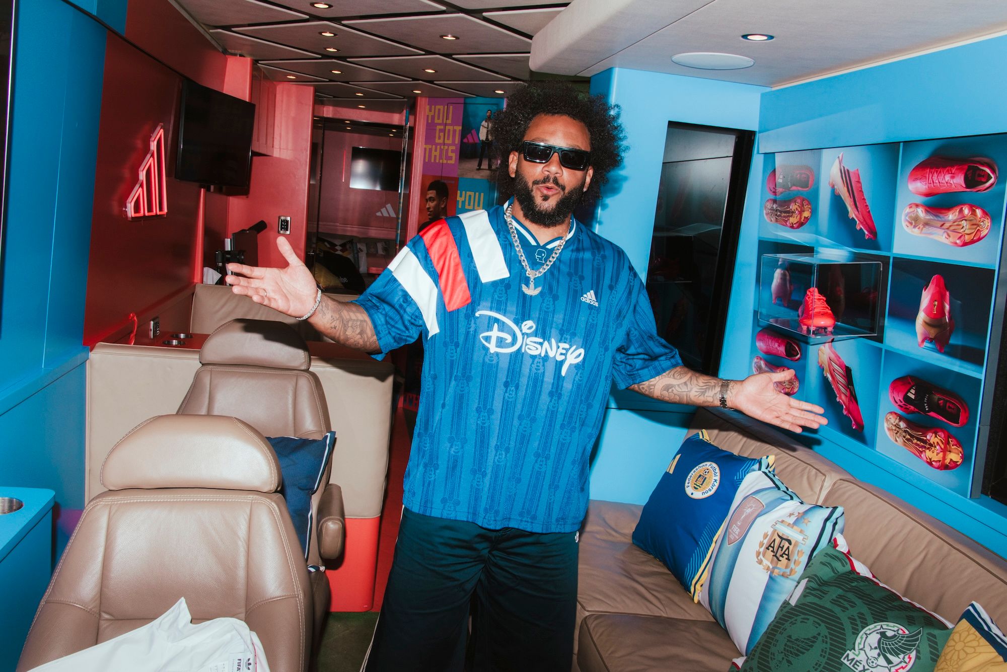 A man wearing a blue Disney-branded jersey stands in a colorful, tech-filled room, holding a smartphone.