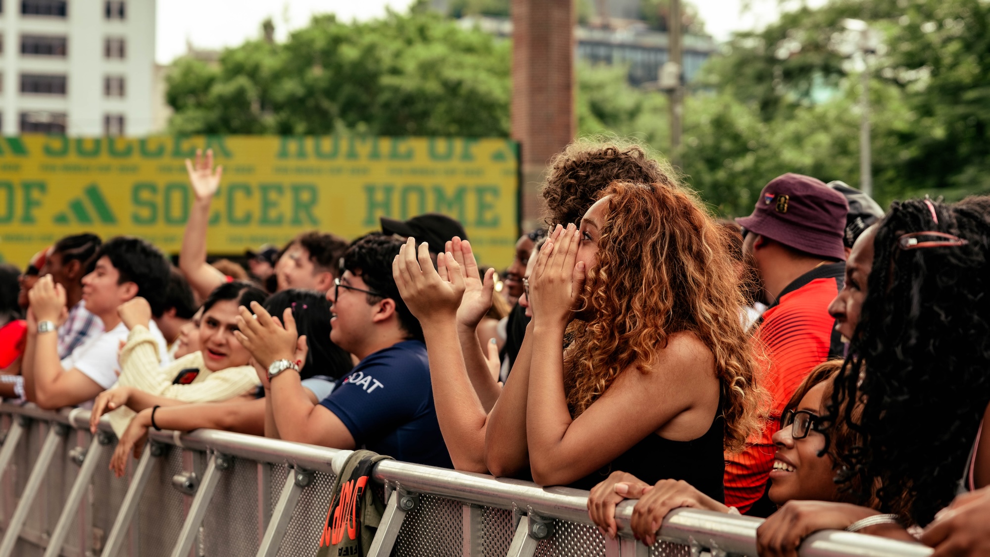 A crowd of people with their hands raised, cheering at a soccer match. A large "SOCCER HOME" banner is visible in the background.