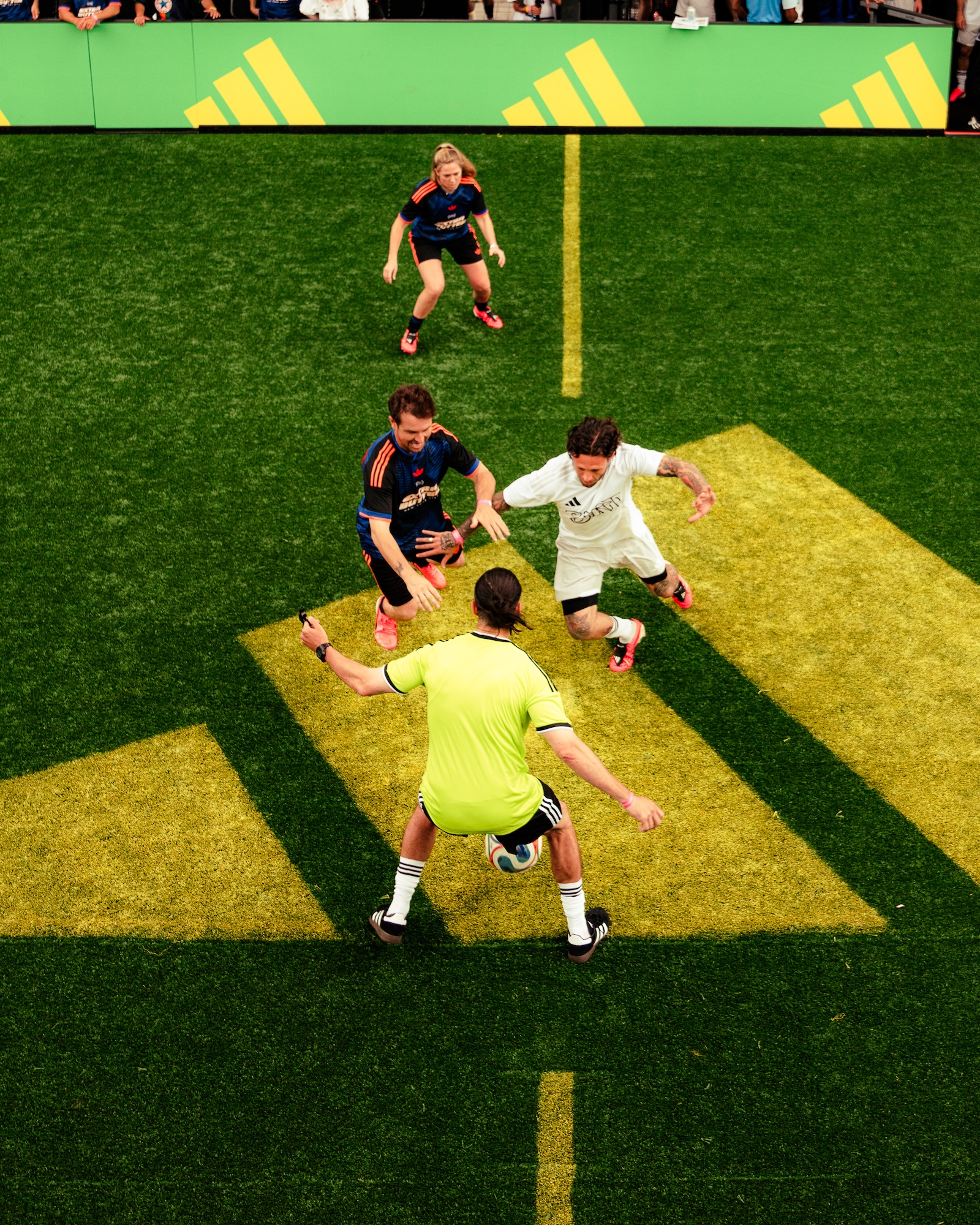 Soccer players competing on a green artificial turf field with yellow markings and Adidas branding.