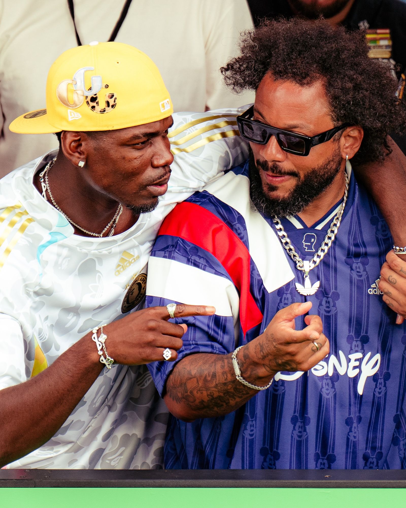 Two men wearing colorful athletic clothing and accessories, one with a yellow hard hat and the other with sunglasses, standing close together and appearing to have a conversation.