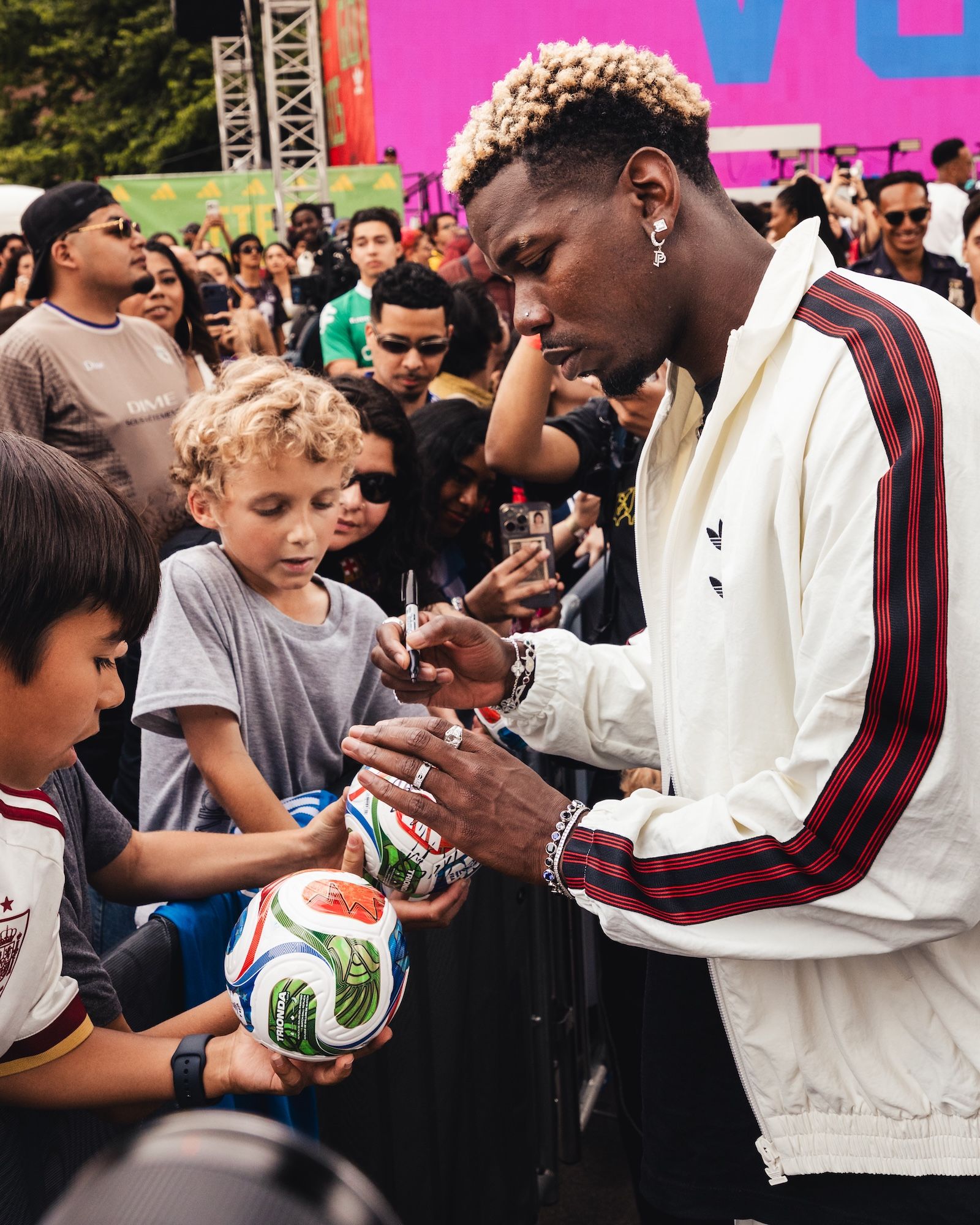 A man with curly hair signing an autograph for a young boy in a crowd at an event.