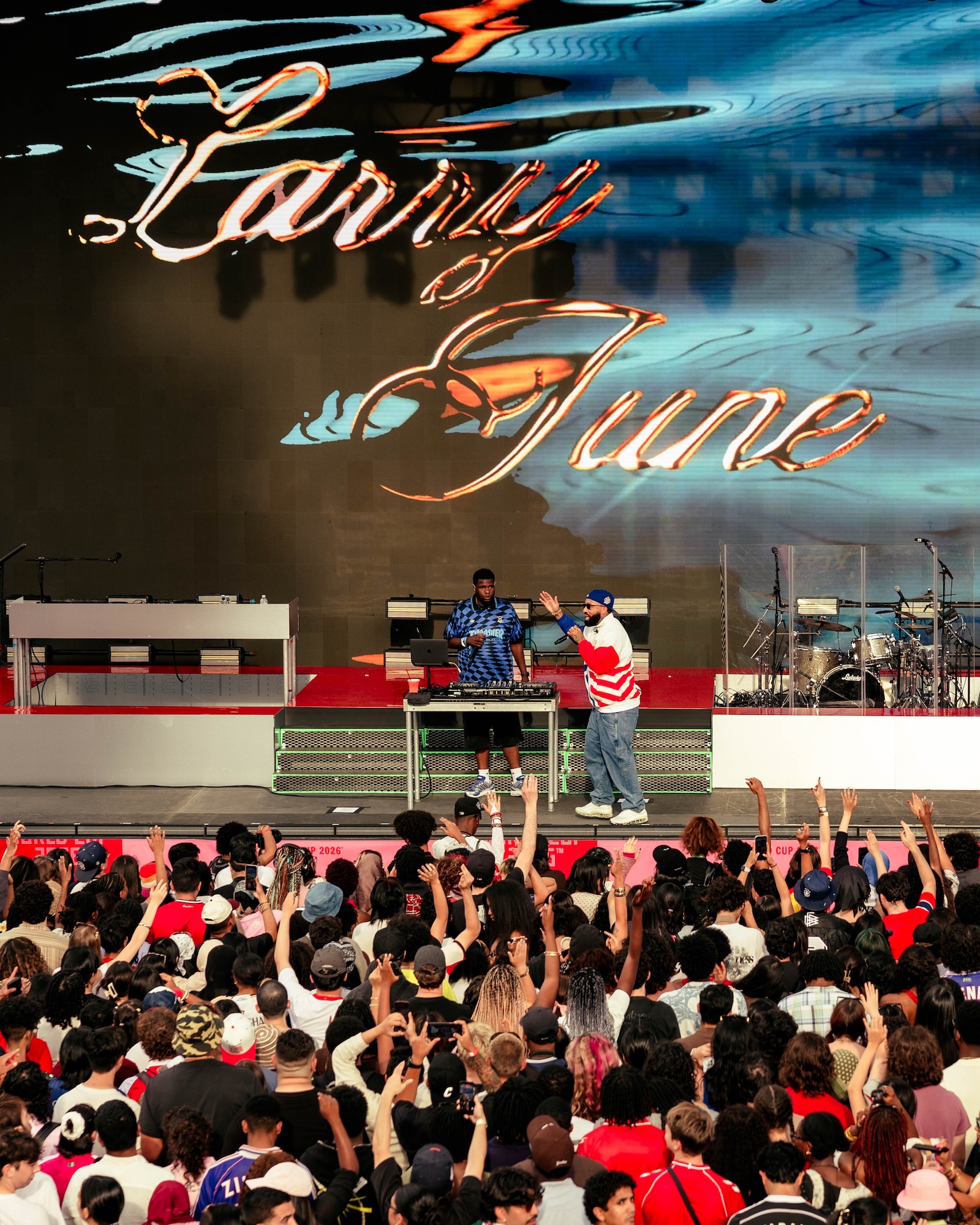 A crowded music festival stage with performers on stage and an enthusiastic audience cheering. The stage backdrop displays the text "Family of June".
