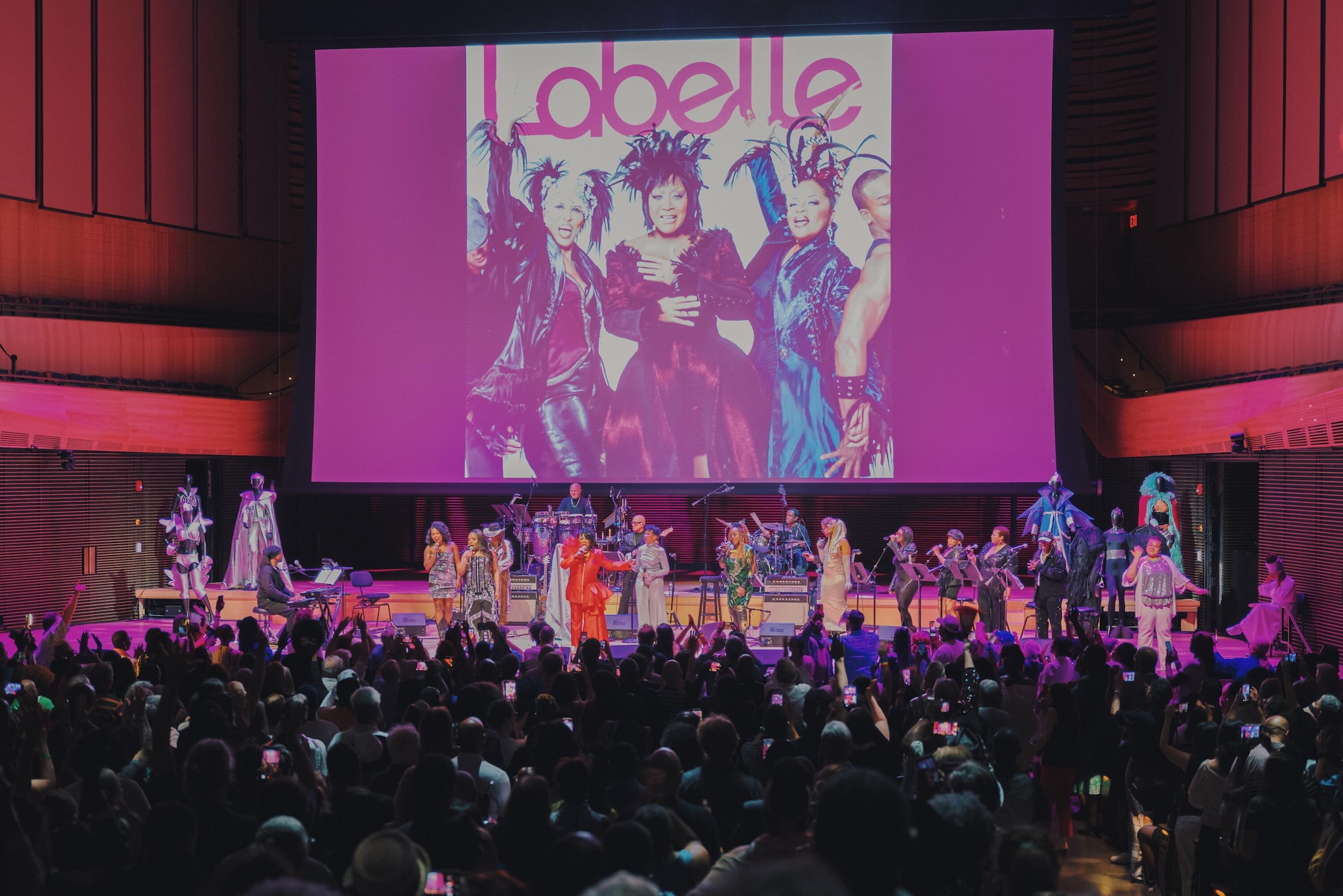 A large crowd at a concert or performance, with performers on stage and a large screen displaying the "Labelle" logo.