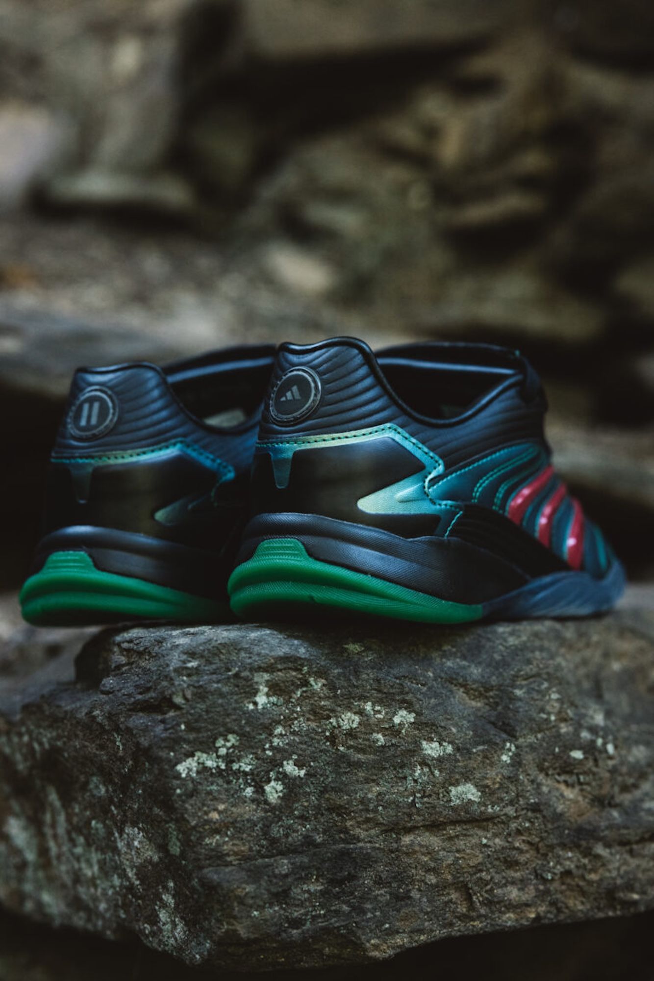 Pair of black and green athletic shoes with wavy patterns, resting on a mossy rock.
