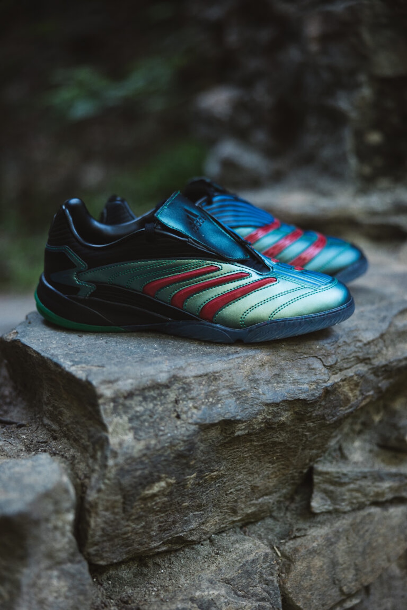 Colorful soccer cleats with red, green, and blue stripes on a rocky surface.