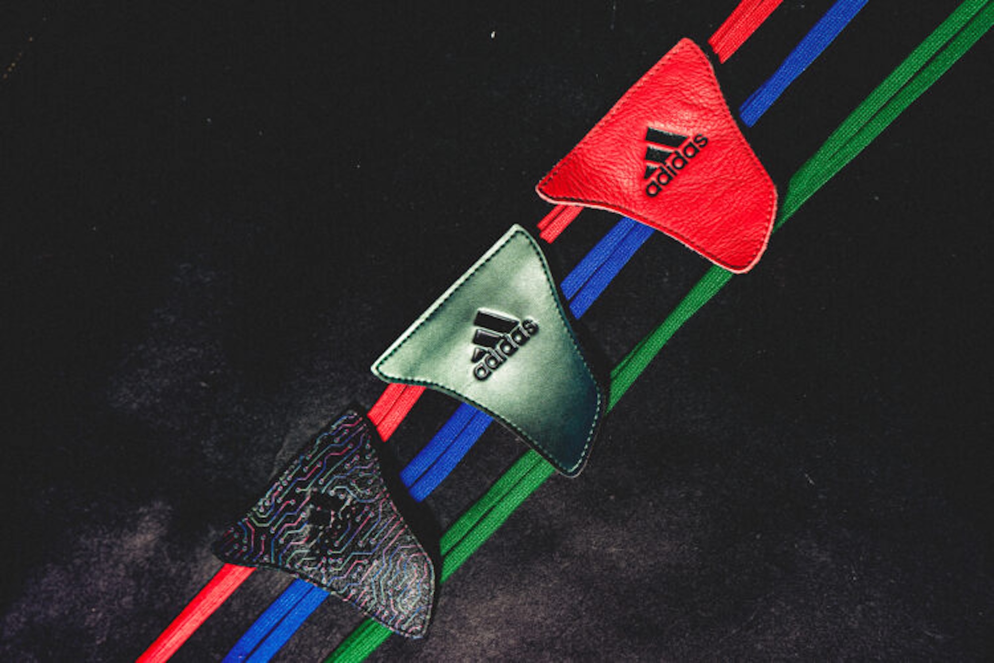 Three Adidas logos on colorful straps against a dark background.